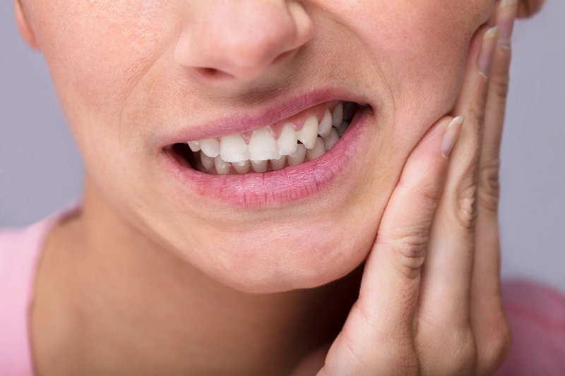 close up of bottom half of woman's face holding jaw as if in pain