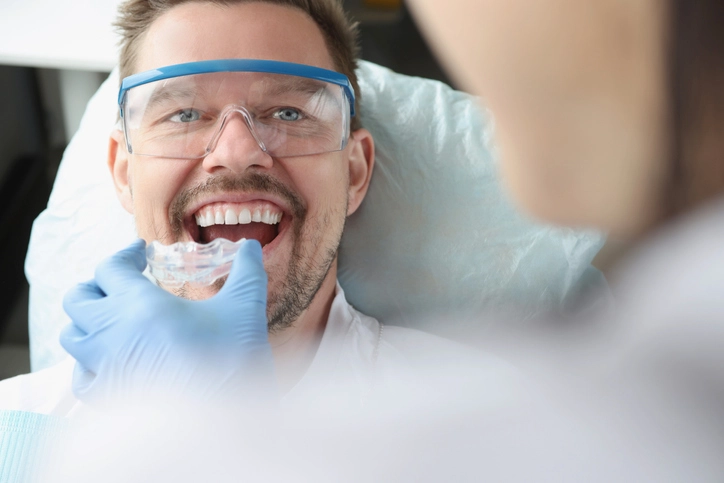 close up of dentist inserting clear aligners into smiling man's mouth
