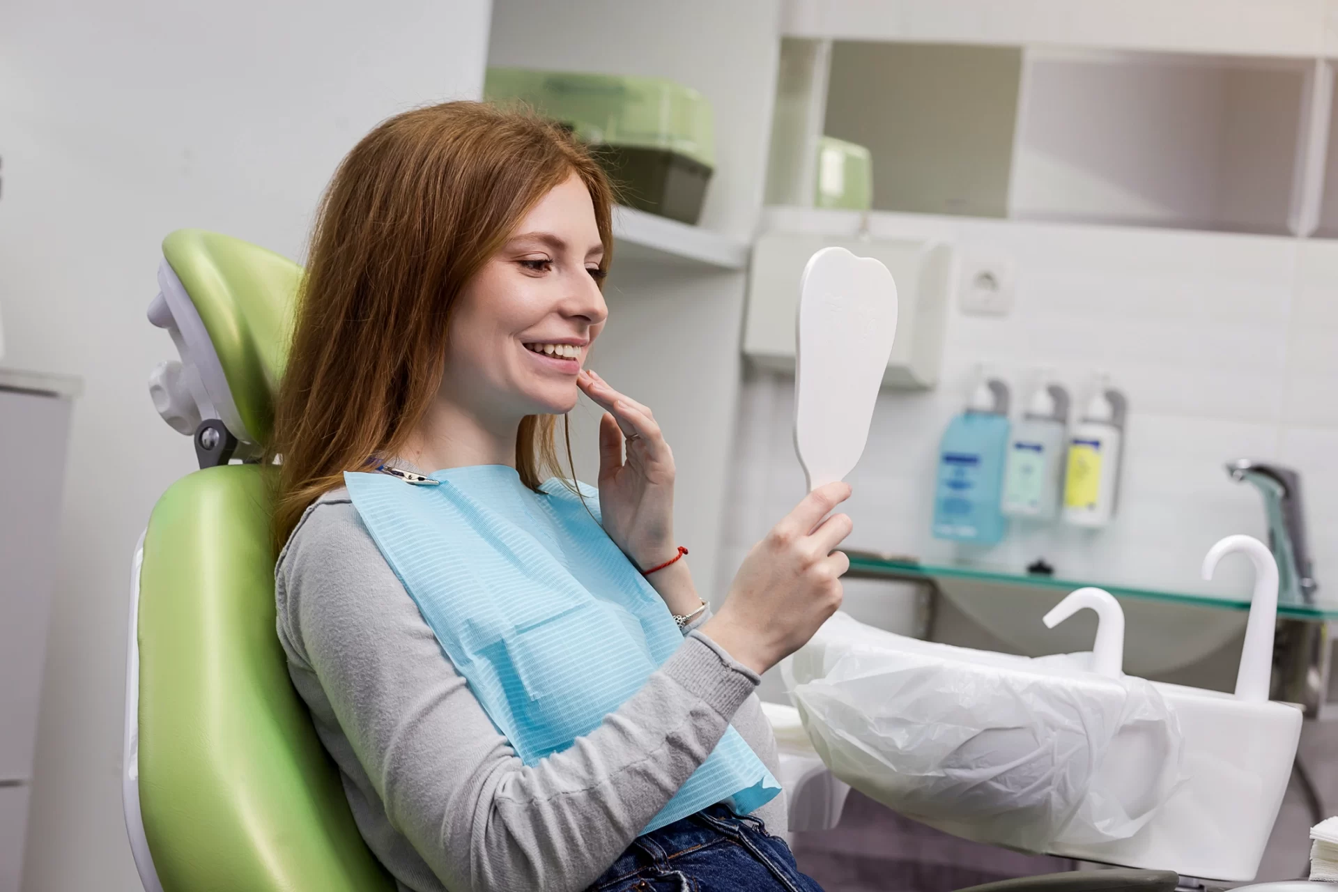pretty young woman smiling at mirror in dentist chair