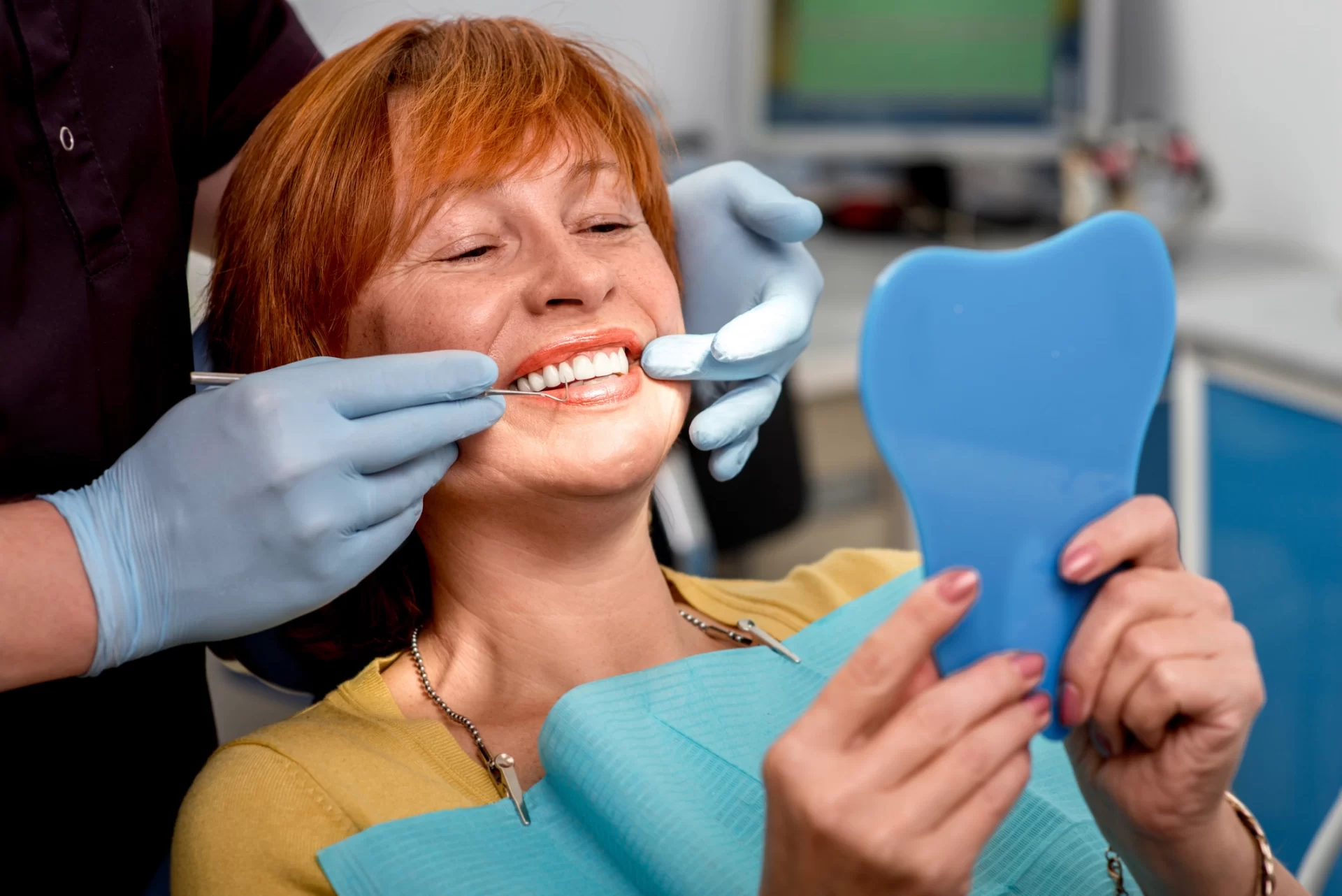 woman smiling in dentist chair while holding a mirror